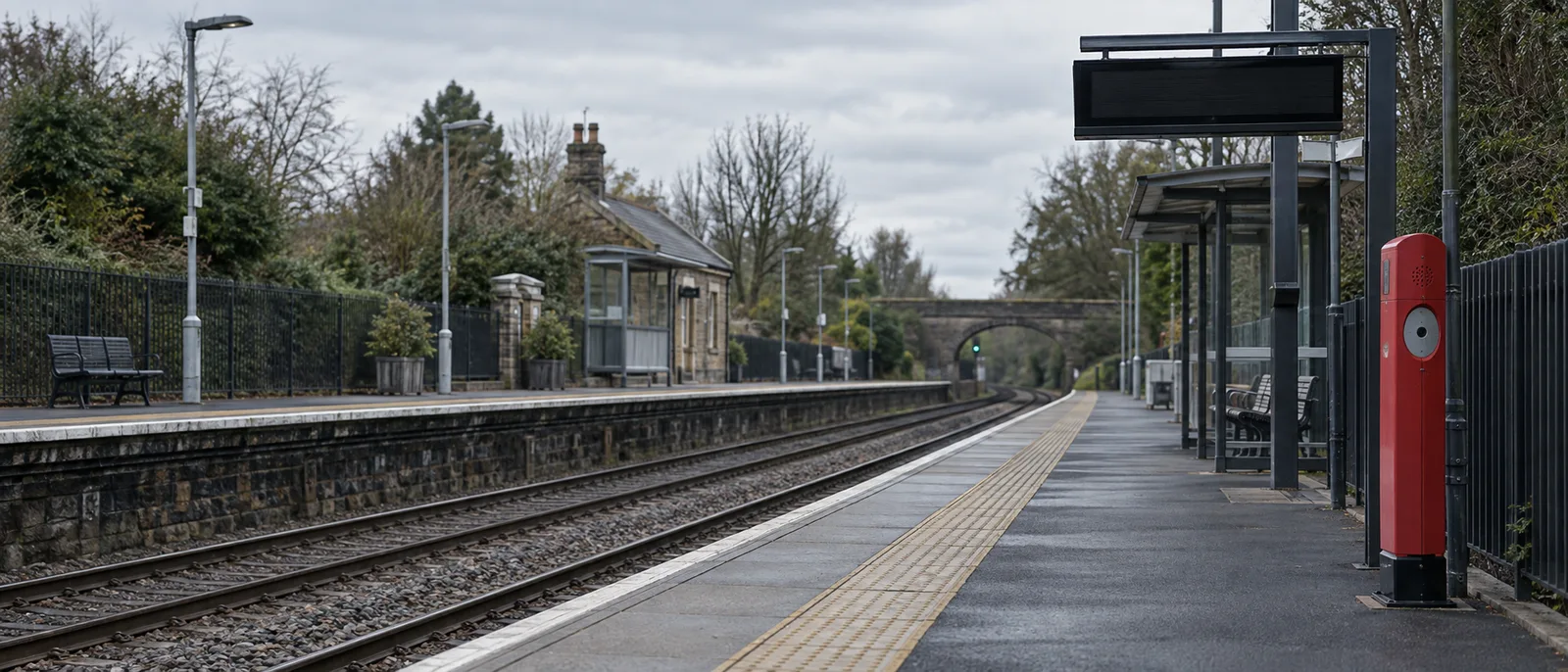 An empty UK railway platform with a red postbox-style help point and a departures screen